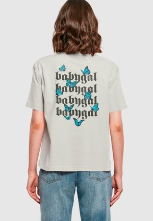 Lys grå oversized t-shirt med et sort og teal sommerfugl grafik og gentagne "babygal" tekst på ryggen. 100% bomuldsstof, korte ærmer.