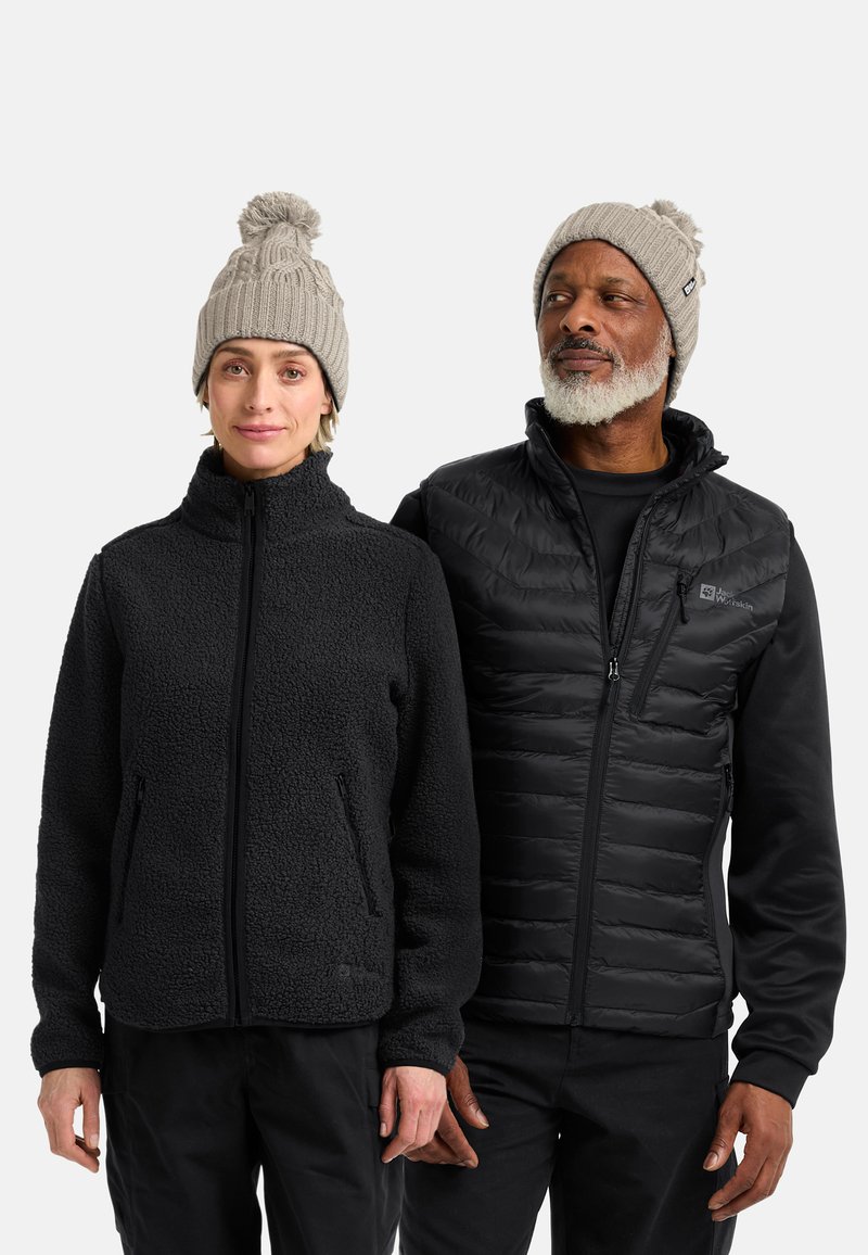 Giacca in pile nera con colletto alto, abbinata a un gilet imbottito nero. Entrambi indossano berretti lavorati a maglia grigi chiari con pon-pon.