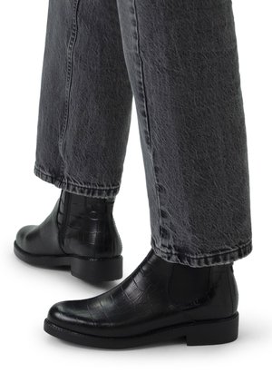 Black leather ankle boots with a crocodile texture, featuring elastic side panels and a low, sturdy heel, paired with gray wide-leg jeans.
