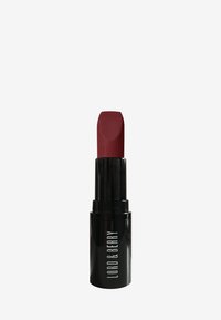 Rouge à lèvres mat de couleur bordeaux profond, contenu dans un tube cylindrique noir avec du texte blanc. Design compact avec une pointe légèrement inclinée pour une application précise.