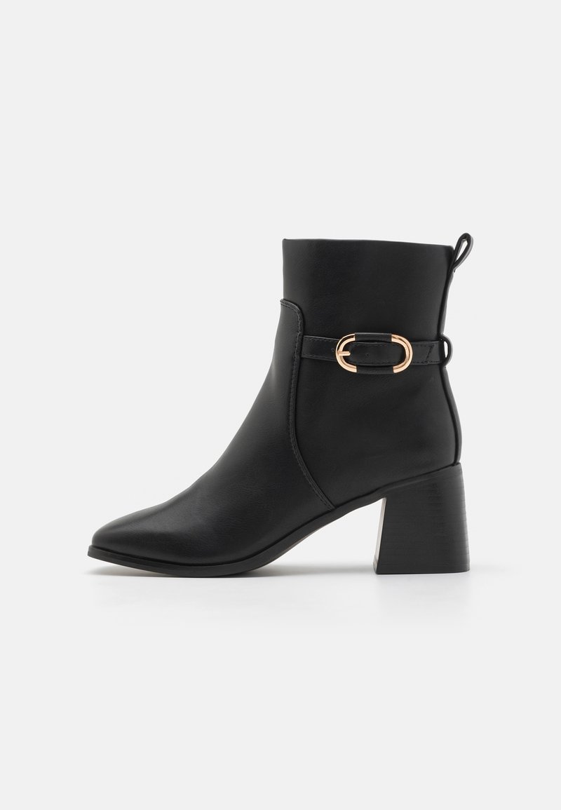 Bottine noire en cuir avec talon bloc, sangle latérale et boucle dorée, vue de profil sur fond blanc.