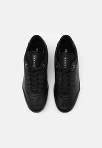 Schwarze Sneakers mit einem glatten Leder-Obermaterial, runder Spitze, Schnürsenkeln und goldenen Akzenten auf der Markenlogo. Strukturierte Sohlen verbessern den Halt.