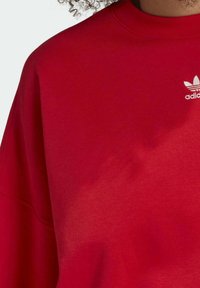 Rode katoenen sweatshirt met een relaxte fit, geribbelde ronde hals en een wit Adidas-logo op de linkerborst. Zachte textuur en minimaal design.
