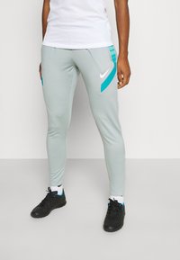 Hellgraue Sportpants mit türkisfarbenen Akzenten, tailliertes Design und Nike-Logo. Verfügt über Reißverschlusstaschen und einen elastischen Bund für zusätzlichen Komfort.