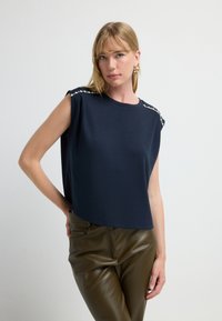 Marineblaue ärmellose Bluse mit lockerer Passform, verziert mit dekorativen silbernen Applikationen an der Schulter und aus weich fließendem Stoff.