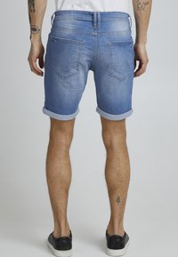Jeansshorts i lyseblå med rullekanter, to baklommer med et subtilt V-formet design. Materialet viser svak falming.