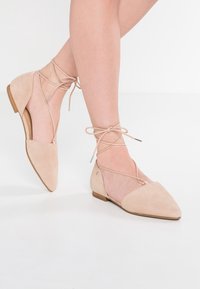 Ballerine nude in suede con punta affusolata, lacci alla caviglia e piccolo dettaglio in argento. Tacco basso e finitura testurizzata per un aspetto elegante.