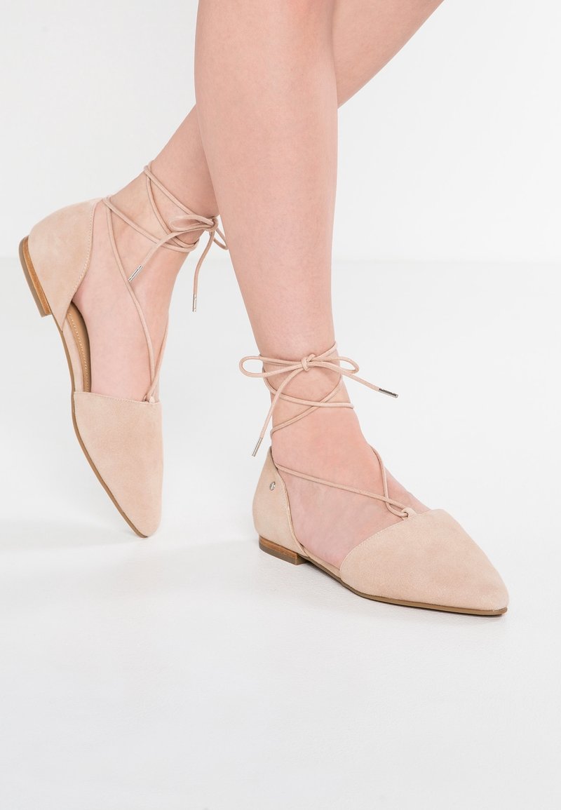 Ballerine nude in suede con punta affusolata, lacci alla caviglia e piccolo dettaglio in argento. Tacco basso e finitura testurizzata per un aspetto elegante.