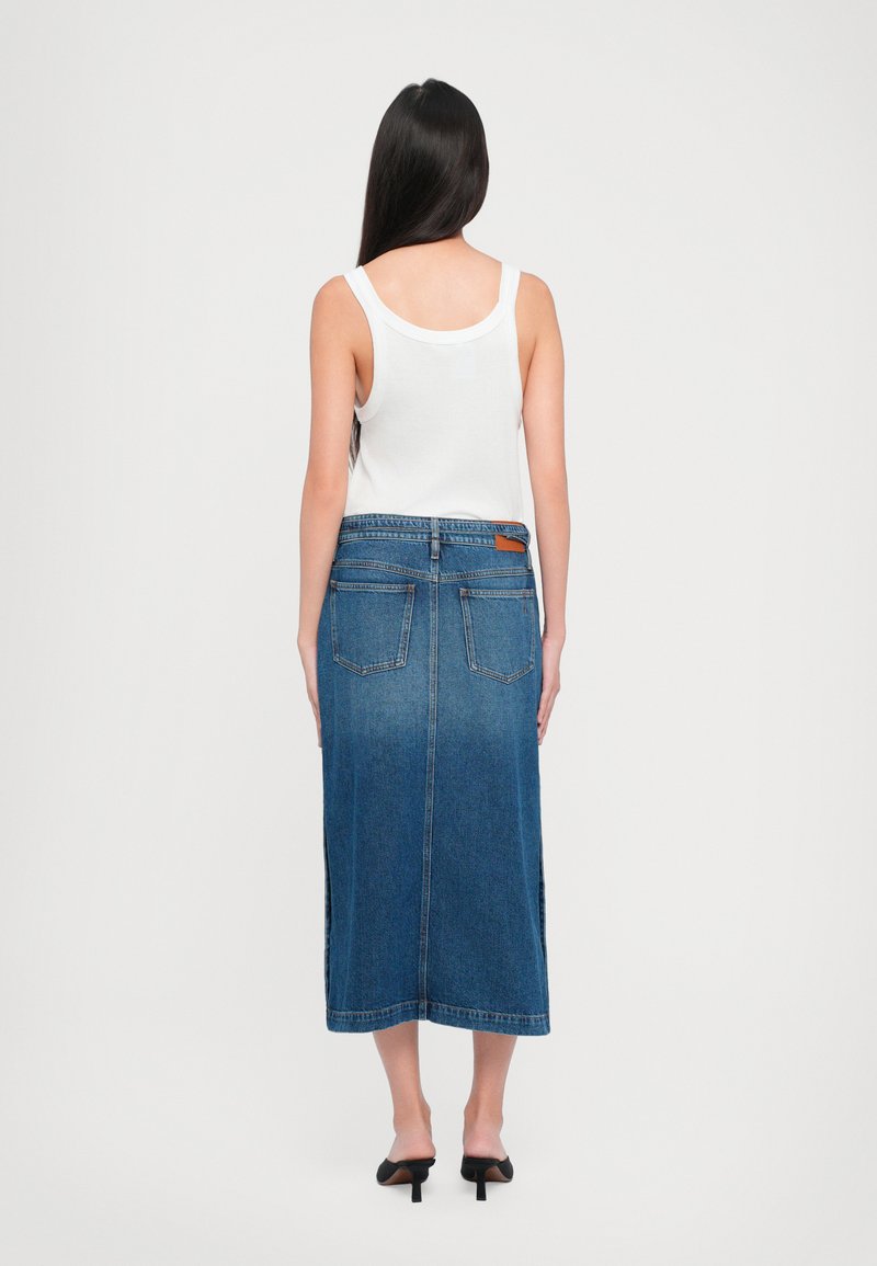 Jupe en denim avec une taille cintrée, dotée de poches arrière, d'une longueur mi-mollet et de fentes latérales pour plus de liberté de mouvement. Assortie à un débardeur blanc.