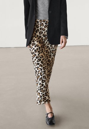 Personne portant une jupe imprimé léopard, un blazer noir, un haut gris et des ballerines noires marchant sur un sol lisse.