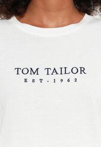 Witte katoenen t-shirt met een ronde hals, zachte textuur en een marineblauwe "TOM TAILOR EST-1962" logo gedrukt op de voorkant.