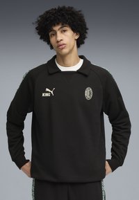 Sort sweatshirt med krave, prydet med hvid "PUMA" logo, "KING" tekst og AC Milan-våbenskjold. Udsmykket med mønstrede grønne sidelister.