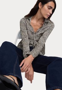 Blusa de estampado de leopardo con escote en V, mangas largas y cintura con cordón. Combinada con jeans de pierna ancha en azul oscuro y zapatos negros de tiras.