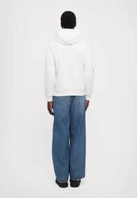 Sweatshirt branca com capuz, com punhos e bainha canelados, combinada com jeans de denim azul de corte largo, com bolsos traseiros e um tom claro.