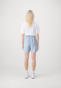 Světlě modré pruhované šortky s elastickým pasem, ve spojení s bílým tričkem, pohled zezadu. Bílé tenisky doplňují tento outfit.