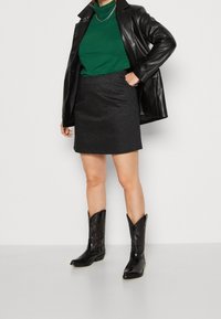 Veste en cuir noire sur un pull col roulé vert, accompagnée d'une mini-jupe noire pailletée et de bottes de cowboy noires avec des détails embossés.