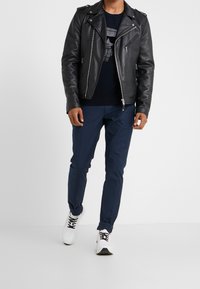 Svart läderbikerjacka med silverfärgade detaljer, mörkblå byxor och vita sneakers. Jackan har dragkedjedetaljer och en figurnära design.