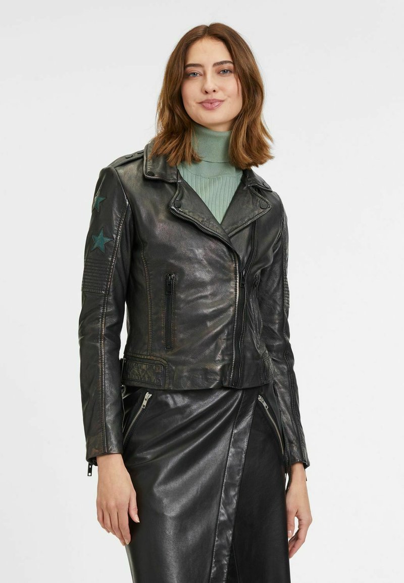 Veste de motard en cuir noir avec une coupe ajustée, accents en étoile verte sur les épaules et détails zippés. Portée sur un col roulé vert clair.
