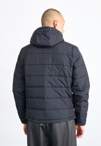 Pufferjakke i mørk navy, med hætte og kviltet design med horisontale sømme. Glat tekstur og elastiske manchetter.