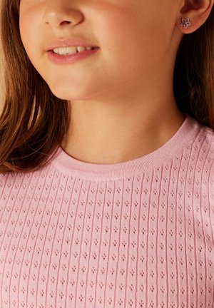 Rosa gerippter Strickpullover mit kleinen Diamantmustern, rundem Halsausschnitt und einem blütenförmigen Ohrring mit lila Akzenten.