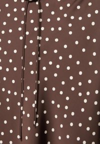 Smeđa tkanina s bijelim nepravilnim točkicama i uskim odgovarajućim vezicama ili vrpcom koja visi okomito.