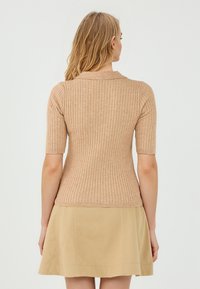 Haut beige à manches courtes à rayures avec une coupe ajustée et un col rond, associé à une jupe beige unie avec des détails de couture.