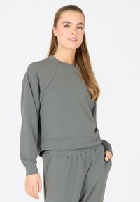 Grå sweatshirt med raglanärmar, rundad hals och textilstruktur. Matchas med grå joggers som har sidofickor och elastisk midja.