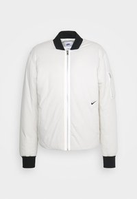 White bomber jacket with black accents; zip closure, ribbed cuffs, and a zip pocket on the sleeve. Smooth fabric with a quilted texture.