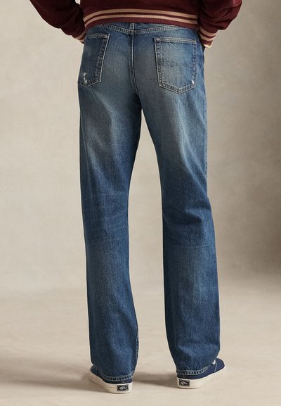 Plave traperice ravnog kroja s dva stražnja džepa i blagim oštećenjima. Nošene s bijelim tenisicama.