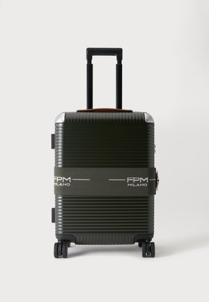 Valise rigide vert foncé avec des rainures horizontales, quatre roues, une poignée noire prolongée et une sangle en tissu gris étiquetée FPM Milano.