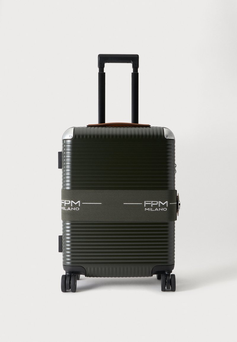 Valise rigide vert foncé avec des rainures horizontales, quatre roues, une poignée noire prolongée et une sangle en tissu gris étiquetée FPM Milano.