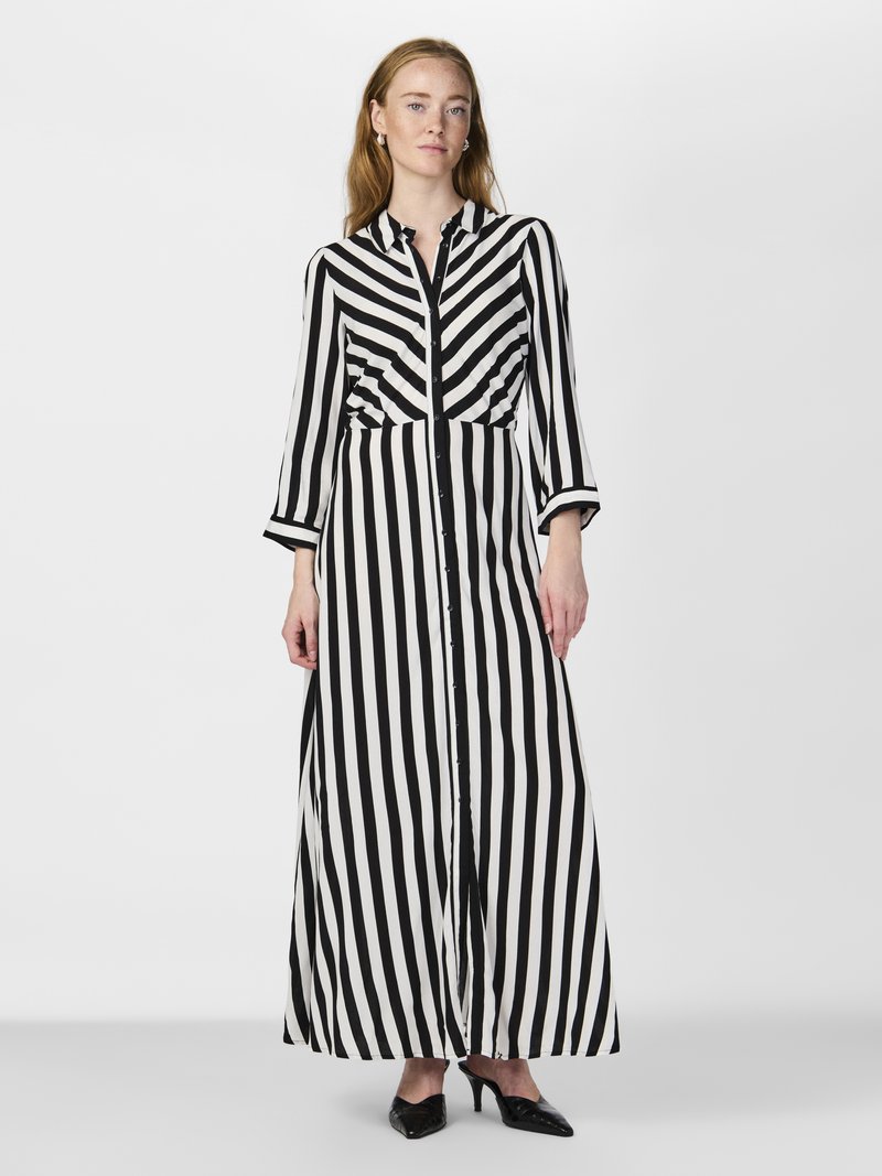 Črna in bela prugasta dolga obleka z gumbom na sprednji strani, ovratnikom in dolgimi rokavi; ima ohlapen kroj in mehak, gladek teksturiran material.