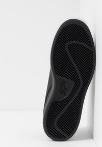 Semelle de chaussure en caoutchouc noir avec un motif de bande de roulement en zigzag et un logo. Bord légèrement surélevé pour le confort et la durabilité. Texture globalement lisse.