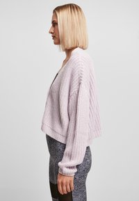 Lys lilla croppet genser i chunky strikk, med løs passform og brede ermer, pairt med mønstrede svarte leggings.