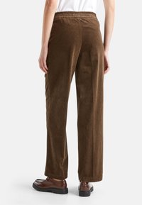 Brązowe spodnie w prążki o luźnym kroju, z elastycznym pasem i pionowym prążkowanym teksturą. Stylizowane z brązowym obuwiem.