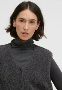 Gray sleeveless vest made of textured fleece with a V-neckline, layered over a long-sleeve dark gray turtleneck.