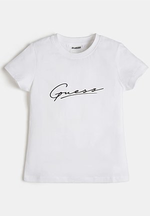 T-shirt blanc à manches courtes avec col rond et texte de logo en cursive noire "Guess" sur la poitrine.