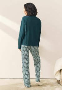 Türkiser Langarmoberteil mit Raglanärmeln, kombiniert mit gemusterten weit geschnittenen Hosen in Grün und Weiß. Weiches Material und entspannte Passform.