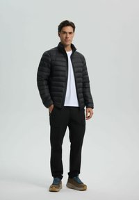 Black puffer jacket with horizontal quilted design, front zipper, and high collar. Paired with black cargo pants and brown hiking shoes.