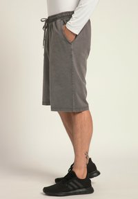 Shorts en coton gris avec une taille élastique et un cordon de serrage, poches latérales et une coupe décontractée. Portés avec des chaussures de sport noires.