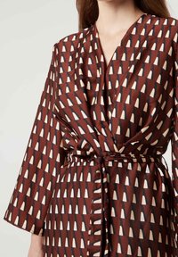 Robe portefeuille marron avec un motif géométrique d'accents triangulaires en crème et marine. Fabriquée dans un tissu lisse avec des manches longues et une ceinture à nouer.