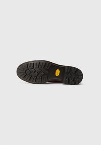 Talpa de cizmă din cauciuc negru cu un tipar profund și un logo Vibram galben, prezentată pe un fundal gri deschis.