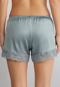 Shorts med spetsdetaljer i en dämpad teal-färg, med en mjuk och slät textur, elastisk midja och dekorativ scallop-kant.