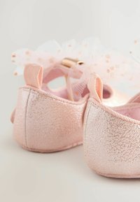 Glänzende rosa Ballettschuhe mit strukturiertem Finish, versehen mit einem Spitzenbogenakzent und kleinen Fersenschlaufen für ein einfaches An- und Ausziehen.