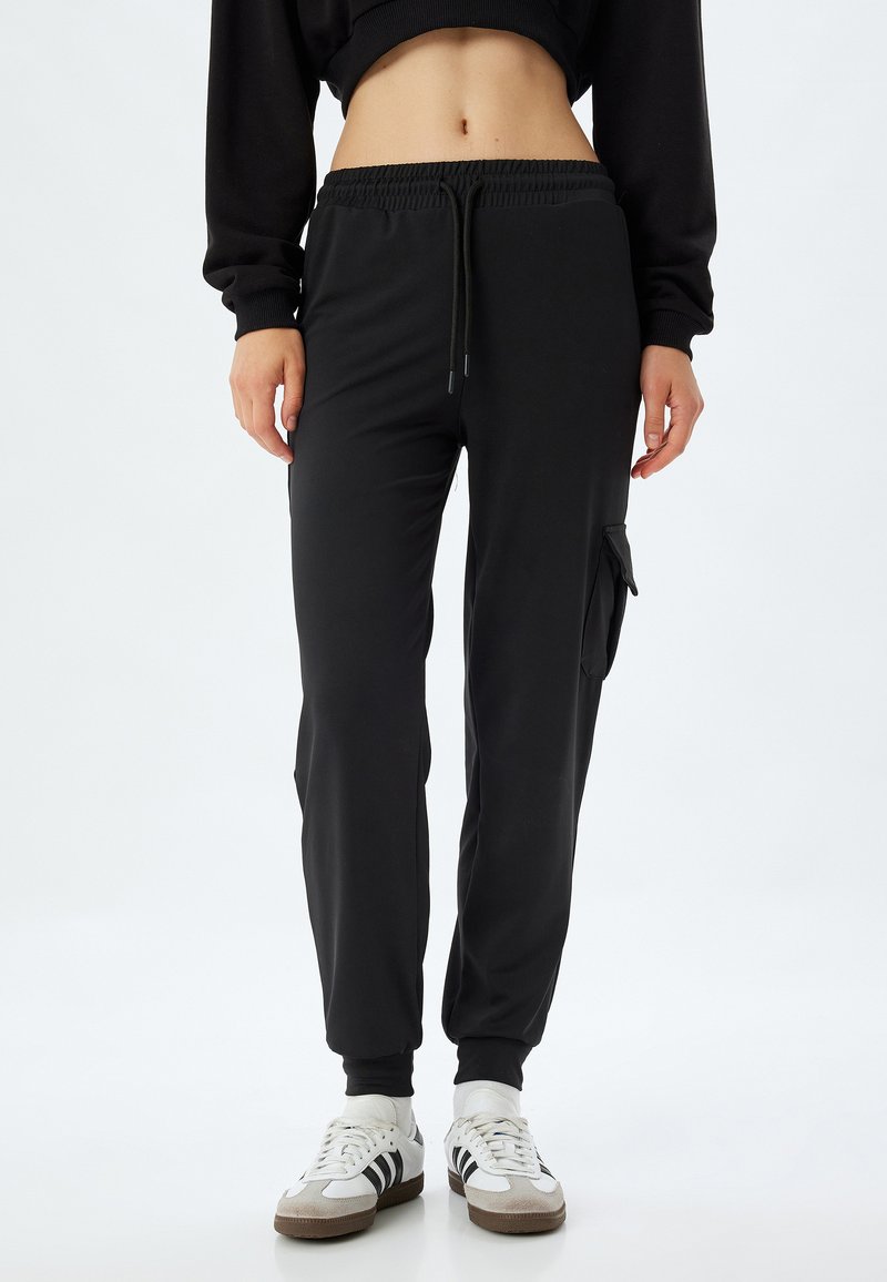 Zwarte sportieve joggers met elastische tailleband en trekkoord, voorzien van zijzakken en taps toelopende boorden. Gemaakt van gladde, rekbare stof.