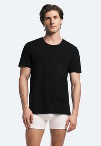 Black short-sleeve t-shirt in cotton fabric, featuring a round neckline and straight cut. Model wears white boxer briefs.