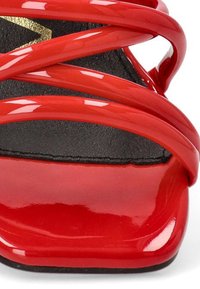 Sandal de tacón alto rojo con acabado brillante de charol, que presenta tiras entrelazadas y una plantilla texturizada negra. La suela plana añade estabilidad.