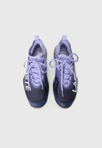 Et par sporty sneakers i lilla og marineblå med snørebåndene knyttet, med dristig hvit tekst på yttersidene, på en enkel hvit bakgrunn.