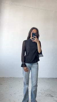 Svart gjennomsiktig topp med høy hals, volangermsermer og hvite kanter, kombinert med lyseblå slengjeans. Enkel og moderne design.