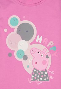 T-shirt rose mettant en vedette un personnage de cochon de dessin animé avec une robe à pois, entouré de bulles colorées et du texte "HEUREUX" dans des polices ludiques.